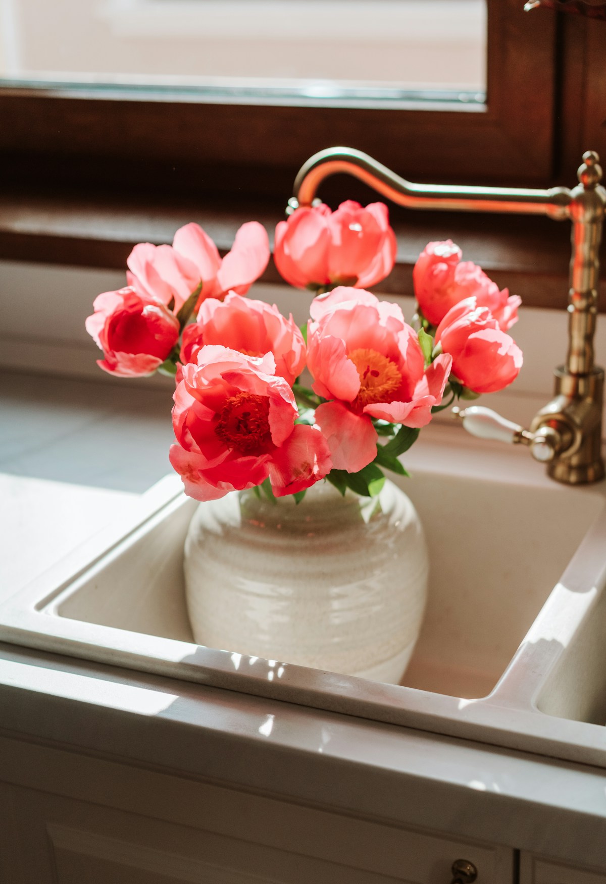 Fresh pink flowers beside a polished brass kitchen tap and a clean white sink